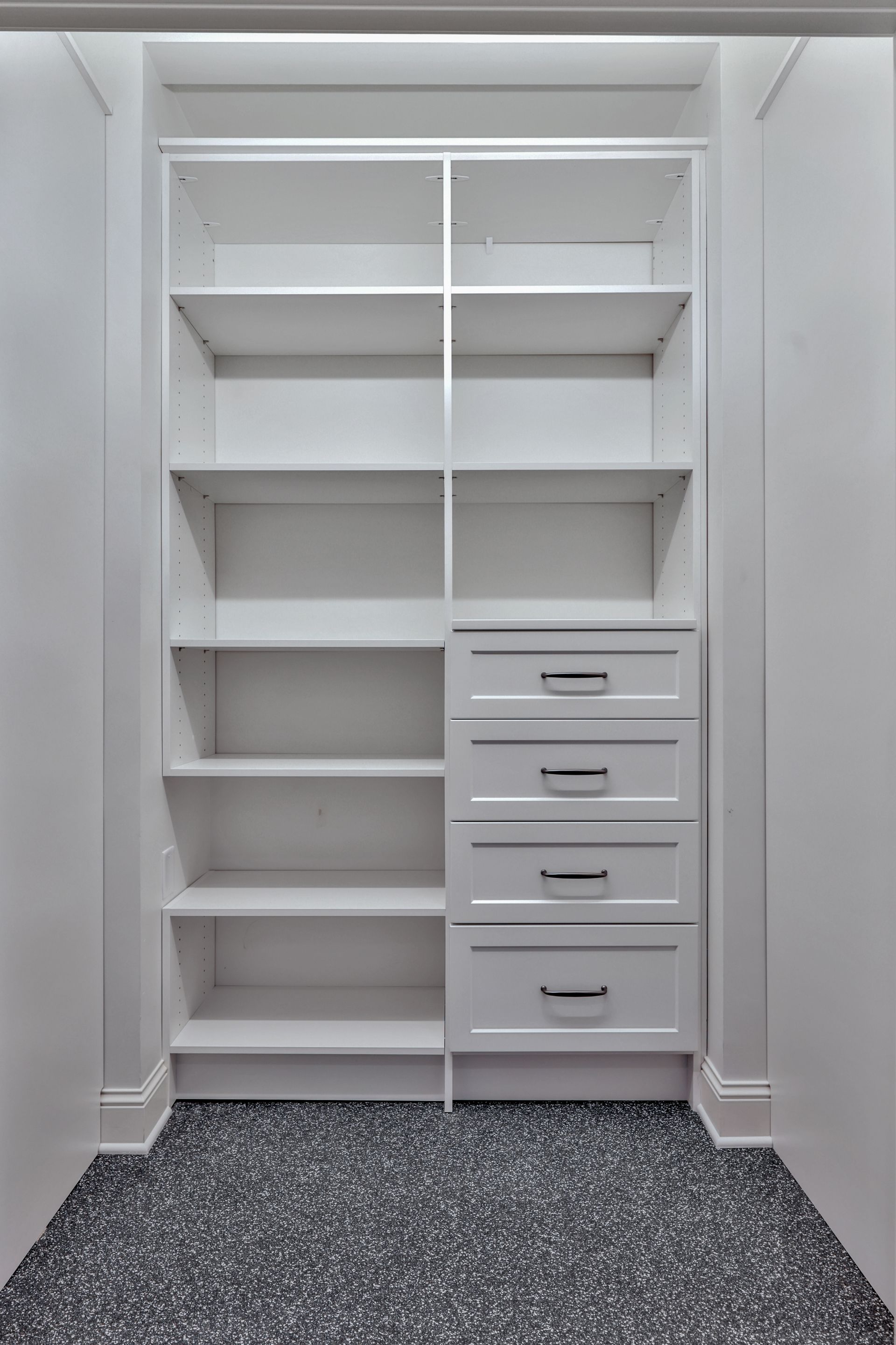 White walk-in closet with built-in shelves, hanging space, drawers, and speckled floor.