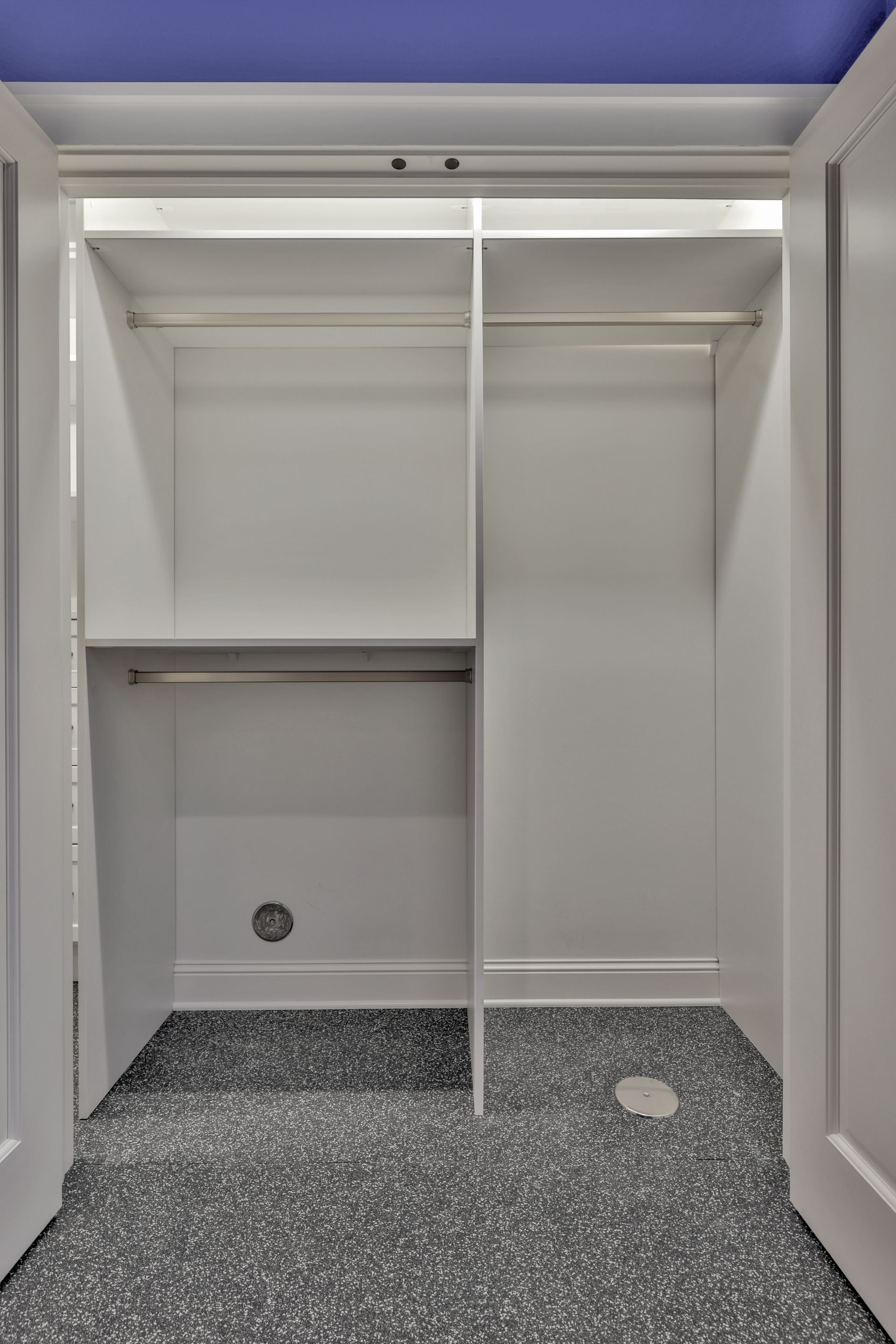 Empty white closet with shelves and hanging rods, gray carpet, and open doors