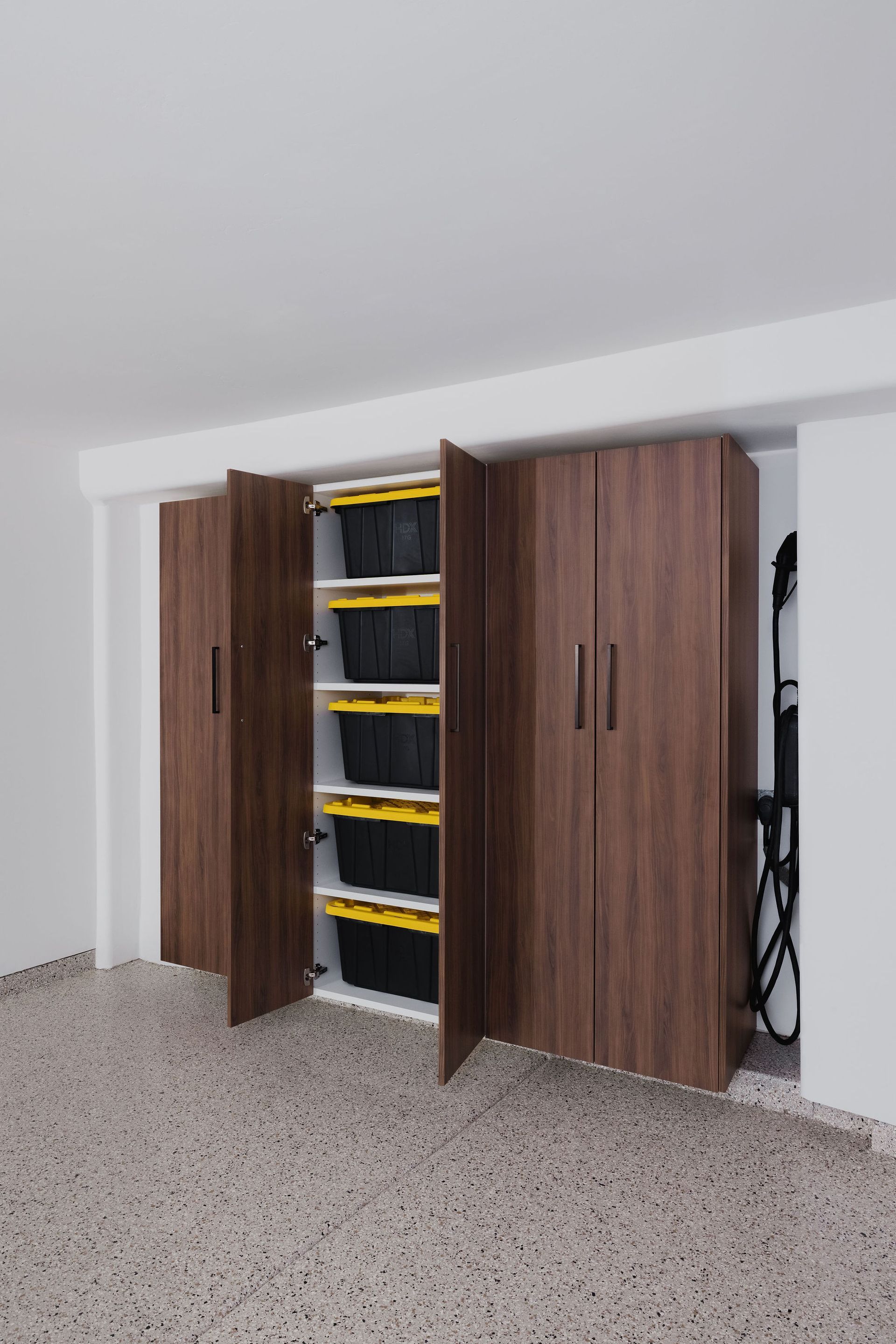 Built-in dark wood cabinets in a garage featuring open shelves holding stacked black and yellow storage bins.