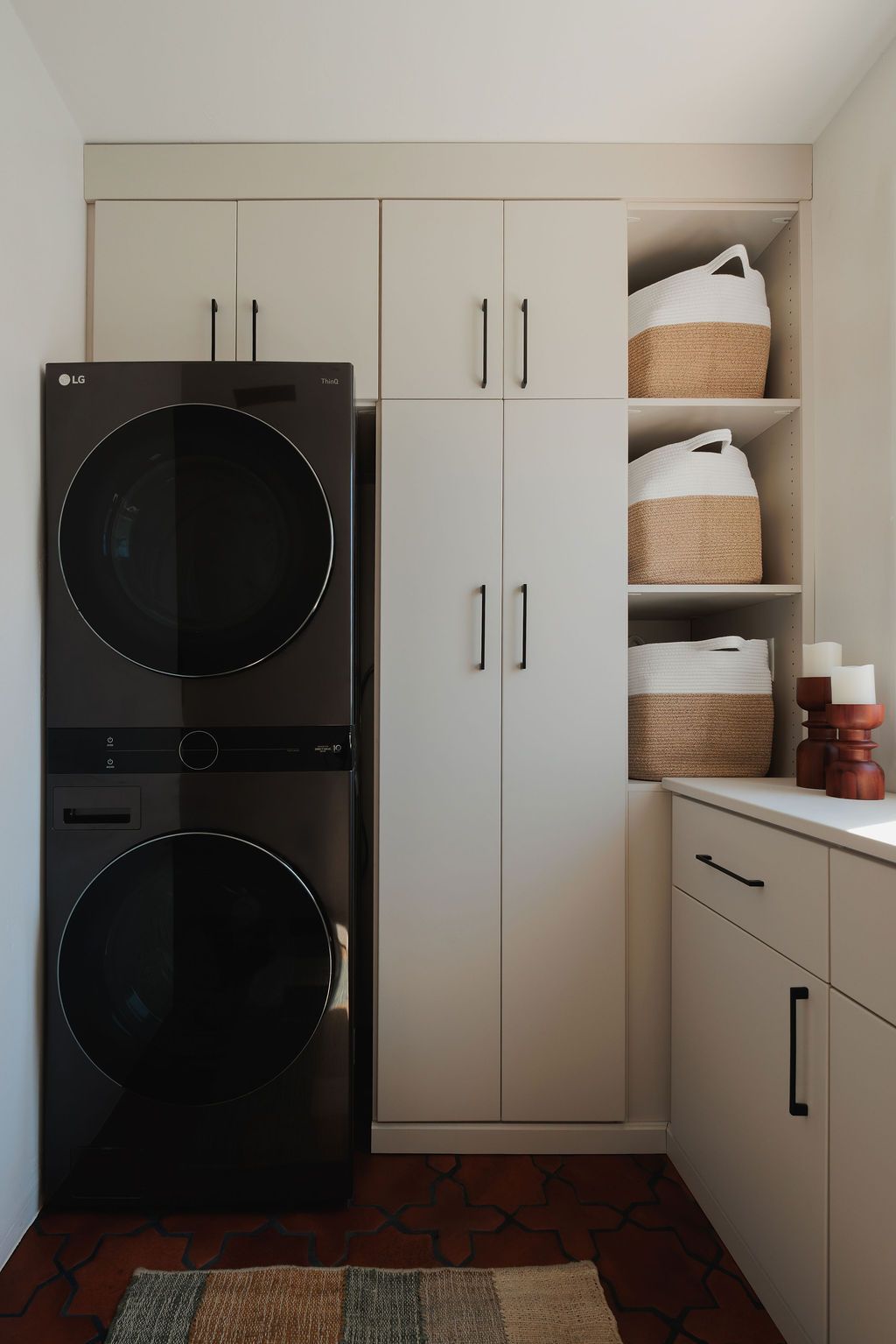 Laundry room with stacked washer and dryer, white cabinets, open shelving, and woven storage baskets