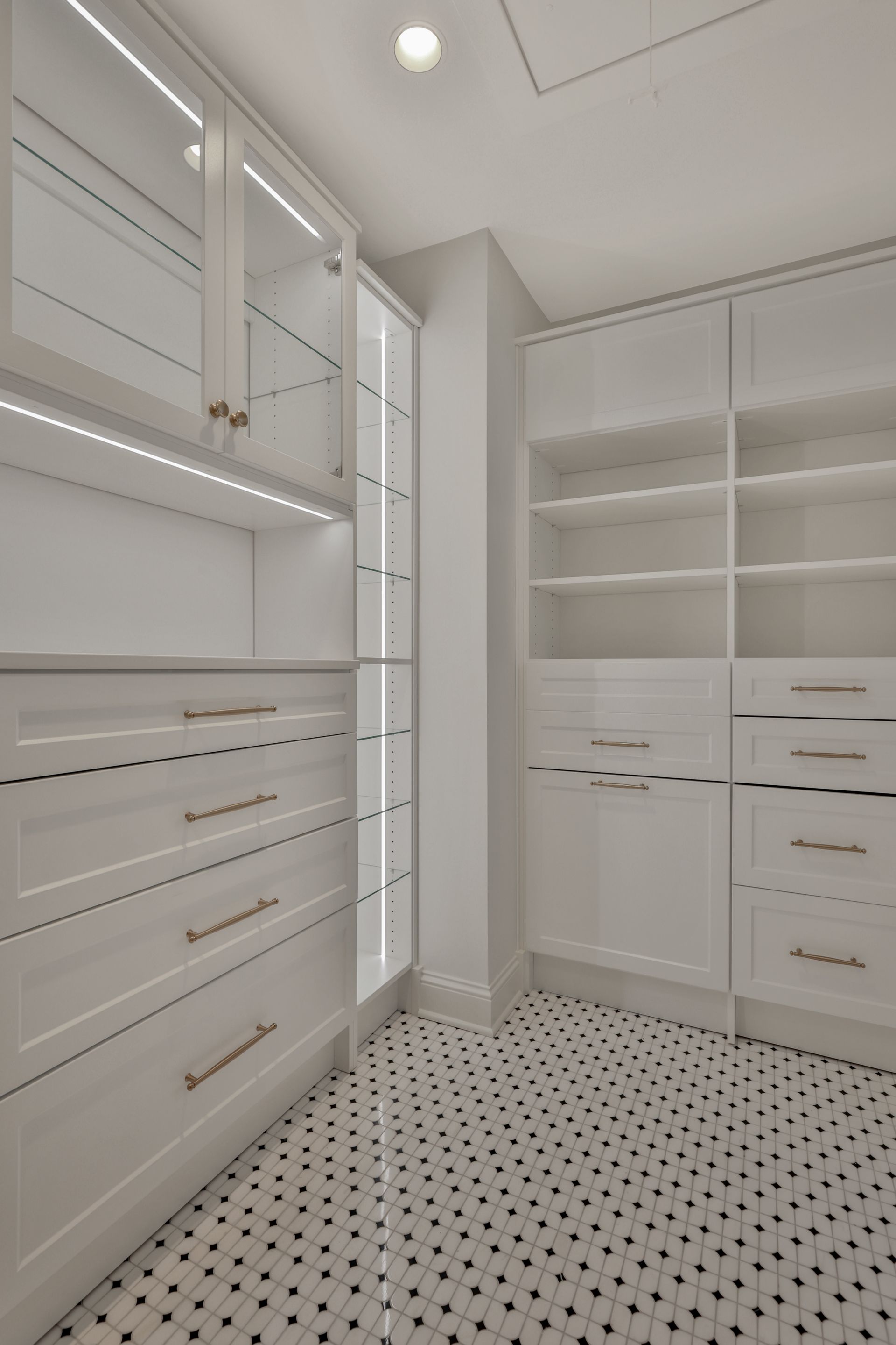 Bright white walk-in closet with built-in shelves, drawers, and black-and-white tiled floor.