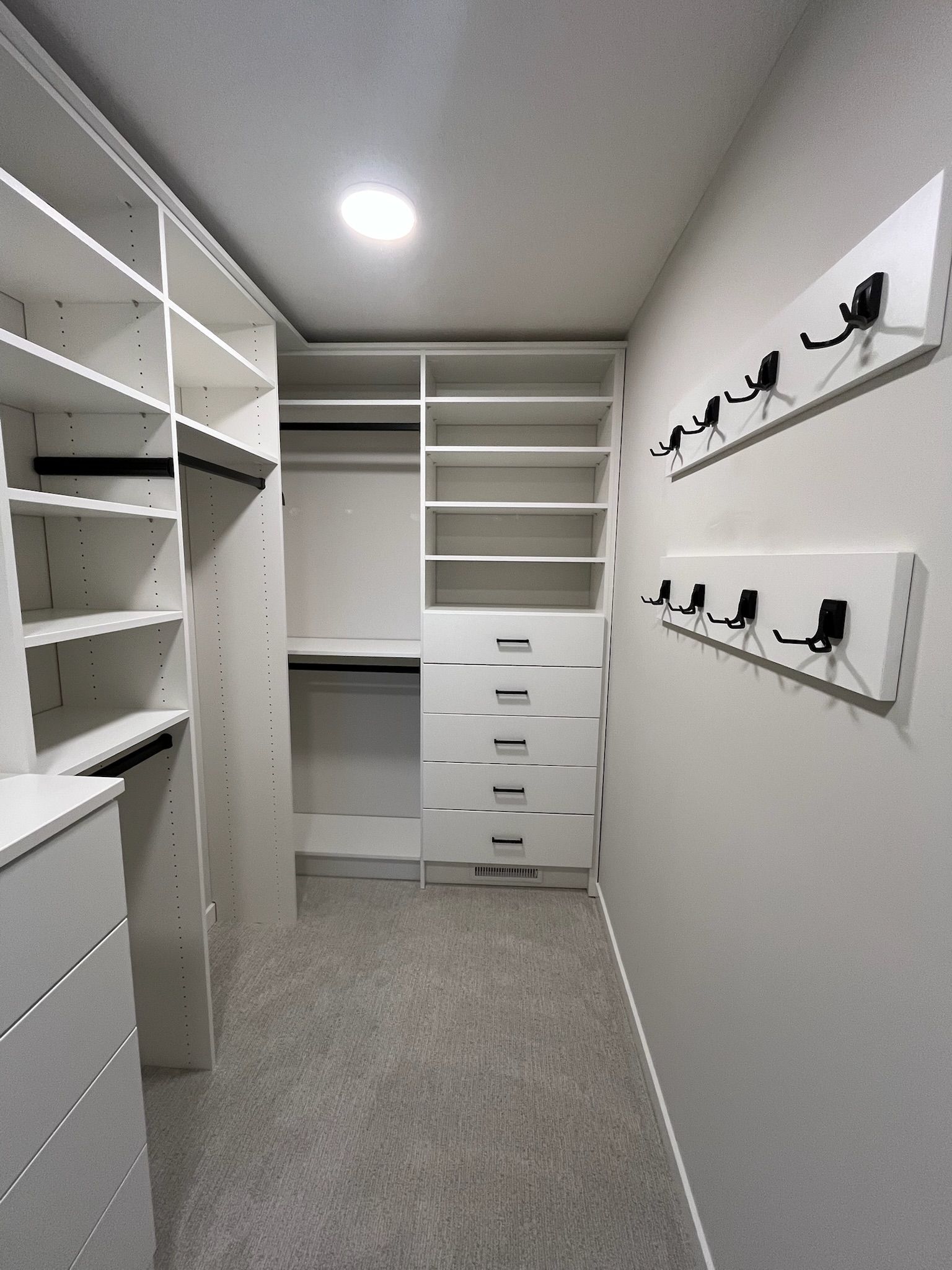 Walk-in closet with white shelving, drawers, and hanging rods on both sides under bright ceiling light