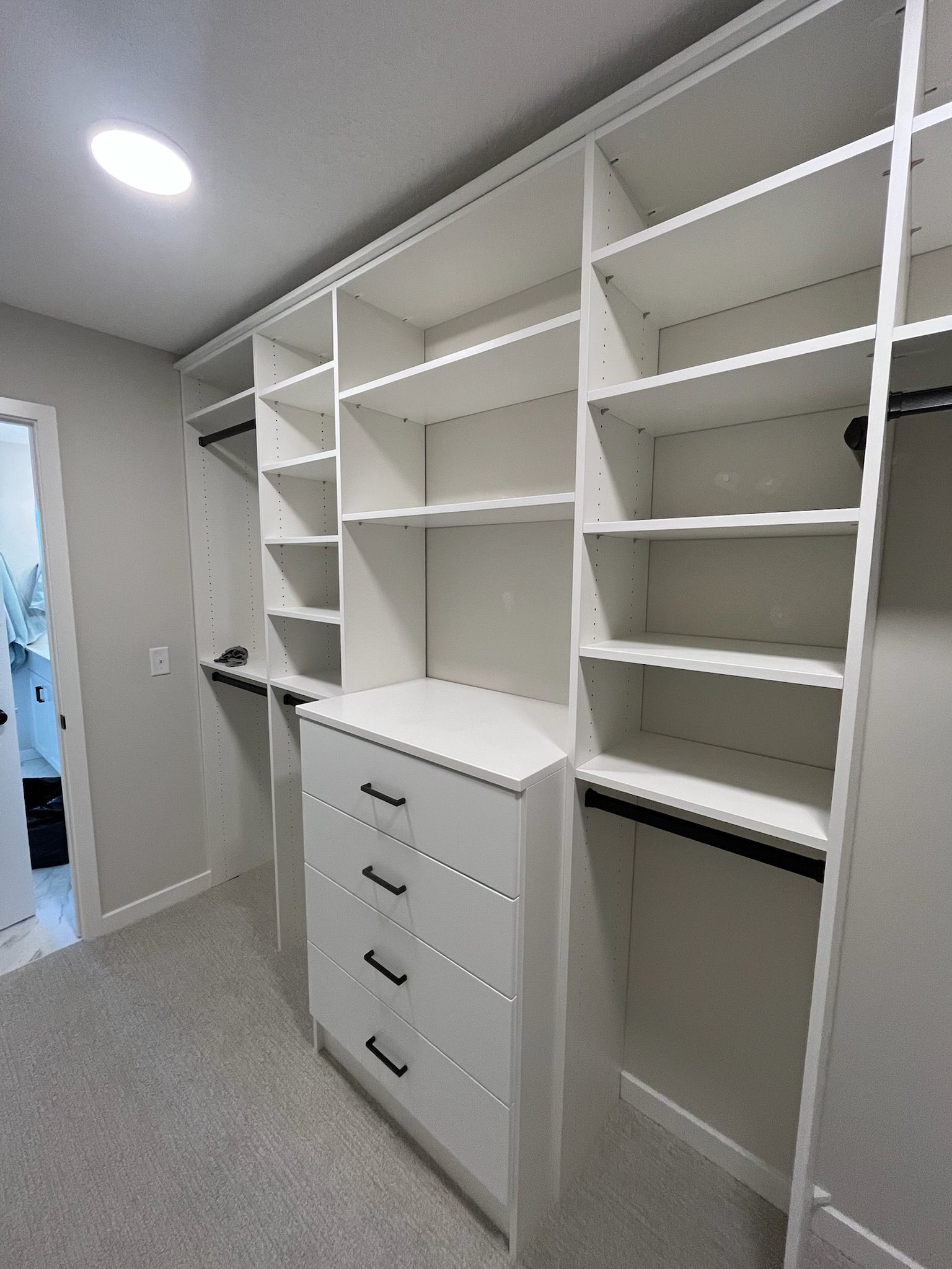 Walk-in closet with white shelves, hanging rods, and drawers on a carpeted floor