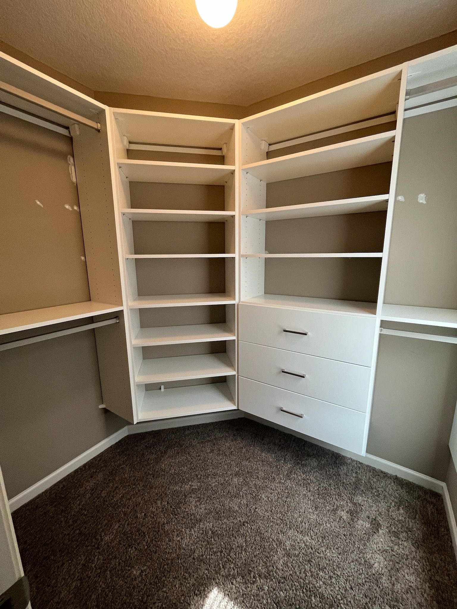 Empty walk-in closet with white shelving, drawers, and beige walls.