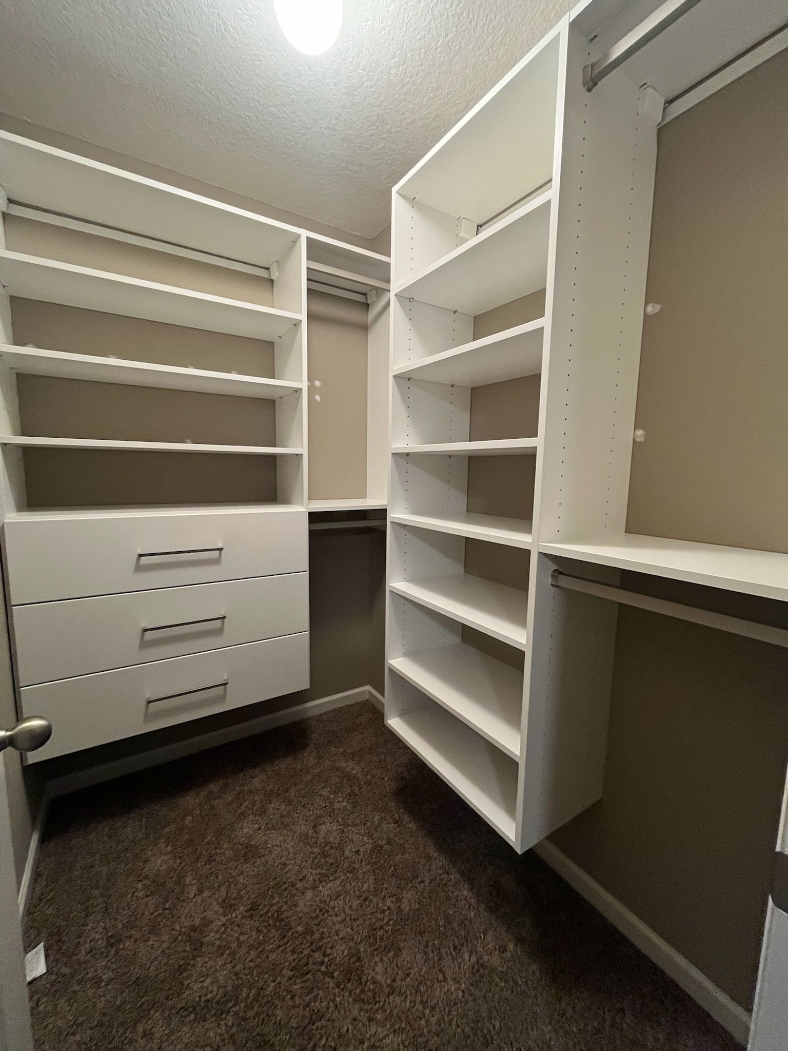 Empty white walk-in closet with built-in shelves, drawers, and hanging rods on beige carpet.