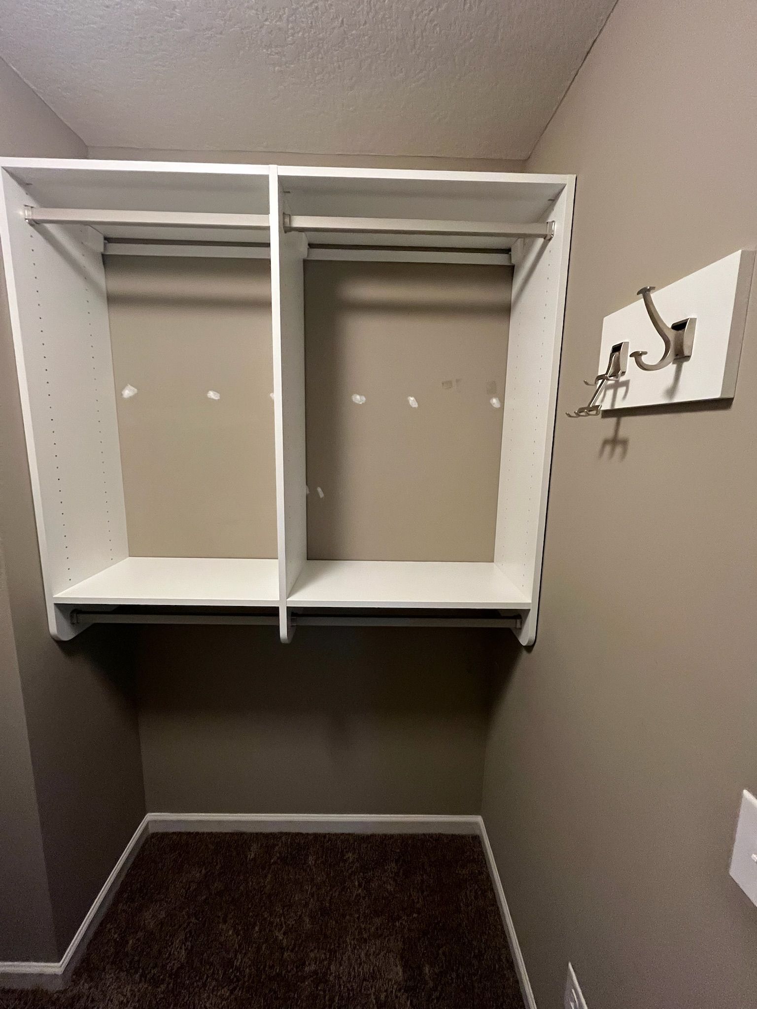 Empty closet with white shelving and hanging rods, gray walls, and dark carpeted floor.