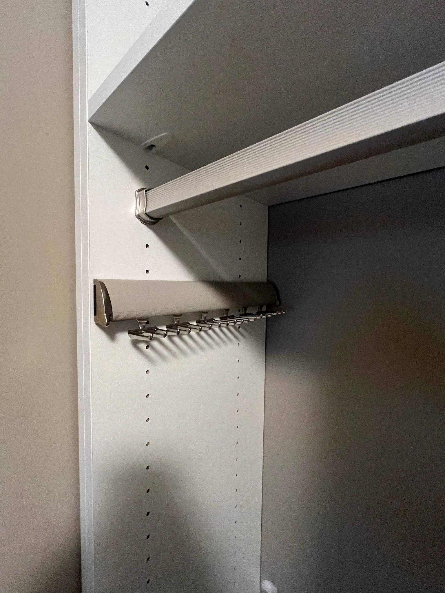 Empty closet interior with white shelves and adjustable side peg holes; metal shelf brackets visible