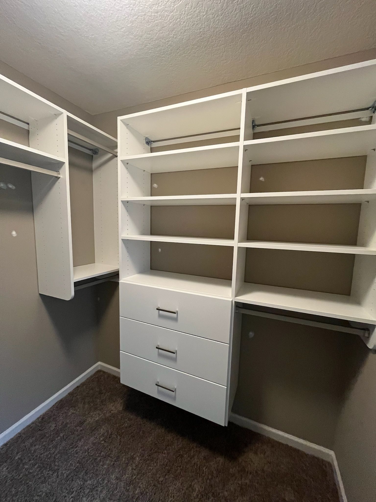 Walk-in closet with white shelves, hanging rods, and drawers over dark carpet.