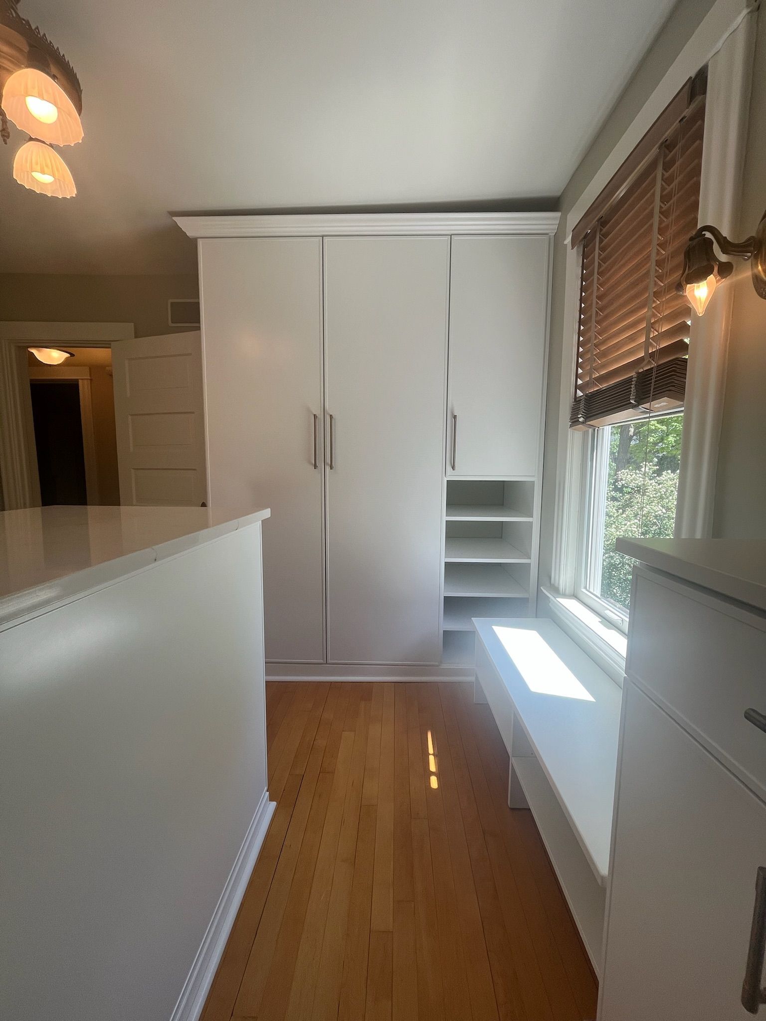 Bright hallway with white cabinets, wood floor, and sunlight by a window with blinds