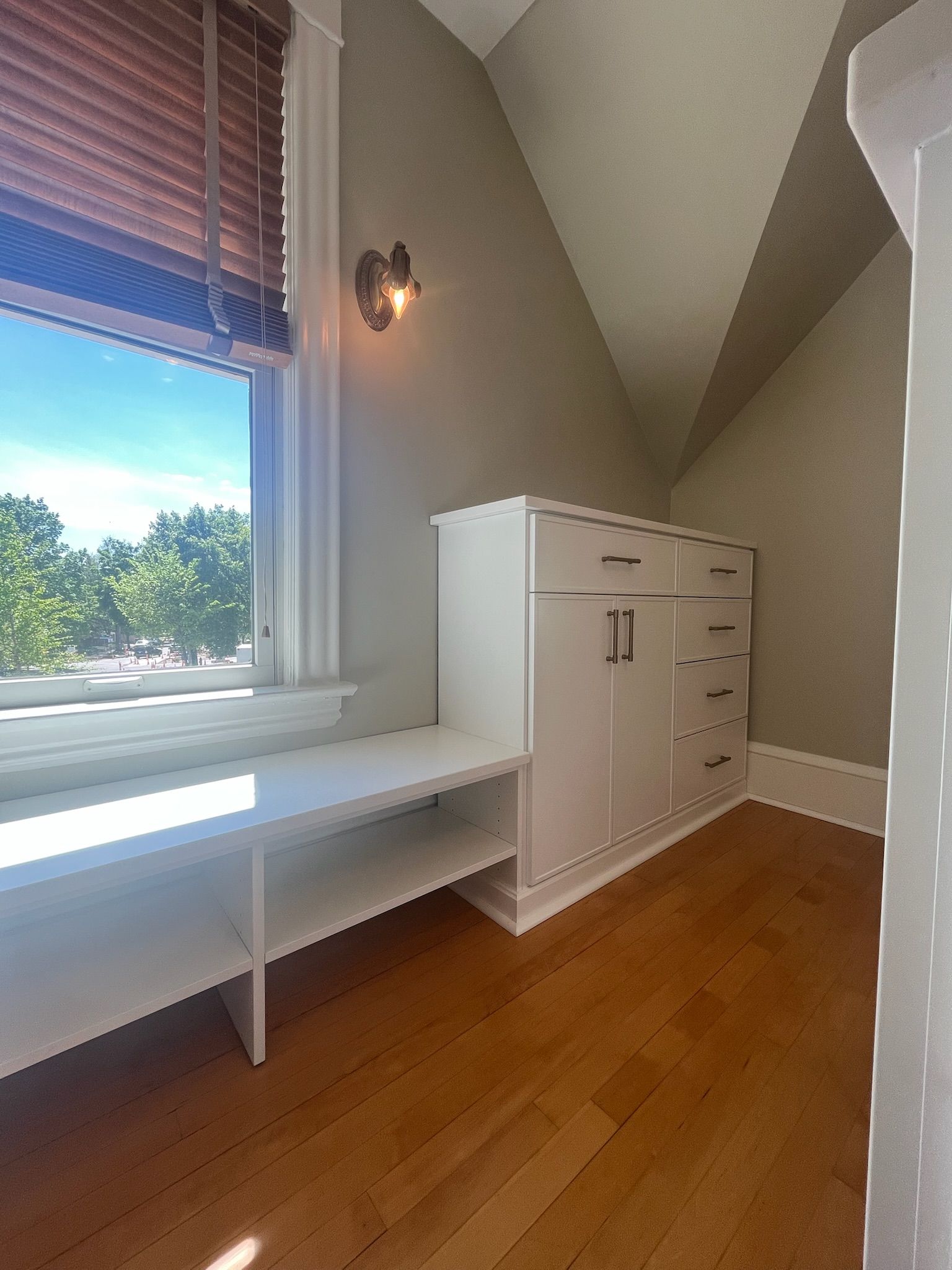 Bright room with a window, white desk, and tall white cabinet on hardwood floor.