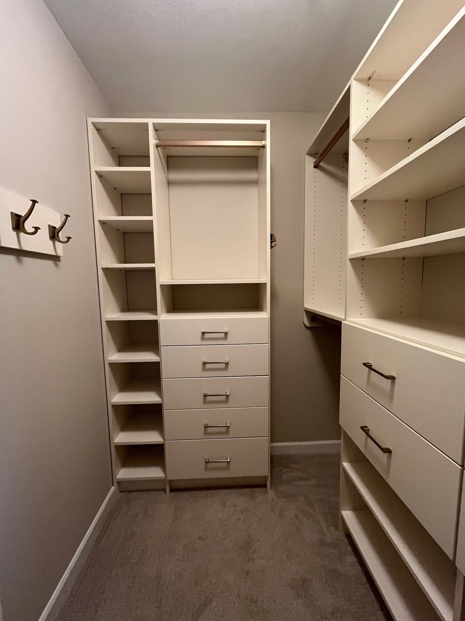 Walk-in closet with white shelves, drawers, and hanging rods on both sides, gray carpet floor.
