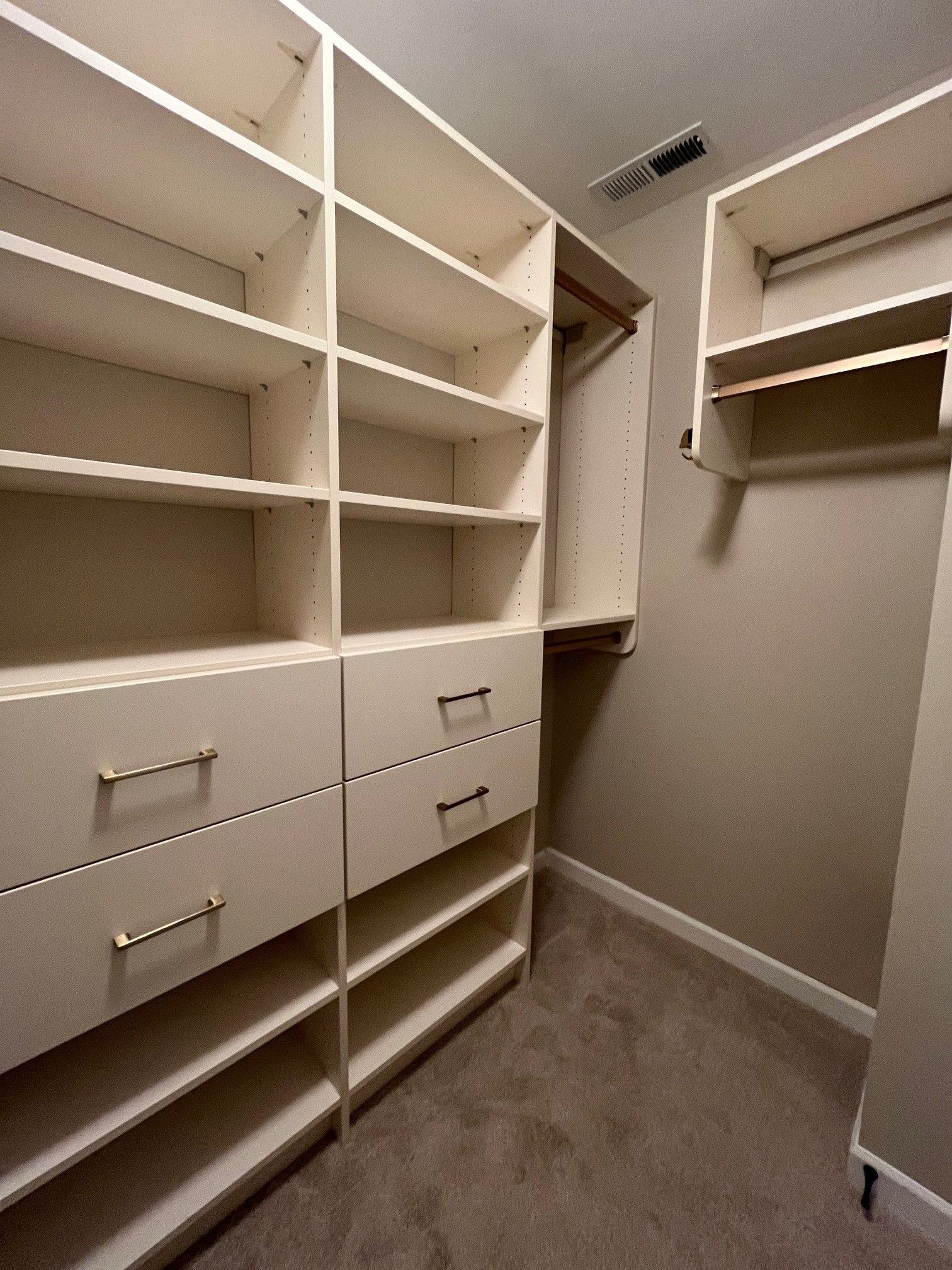 Walk-in closet with white built-in shelves, drawers, and hanging rods on both sides.