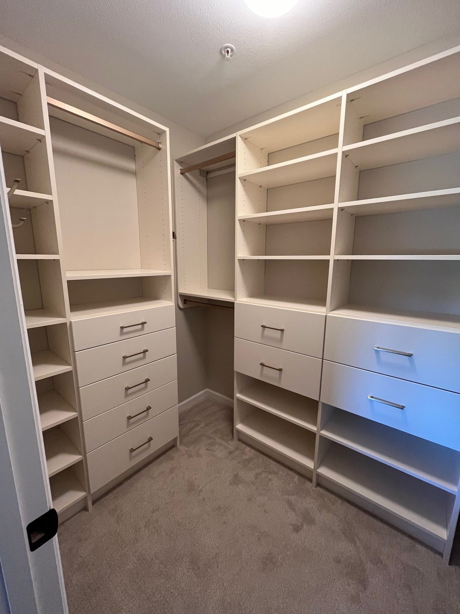 Empty walk-in closet with white built-in shelves and drawers, beige carpet, and hanging rods.
