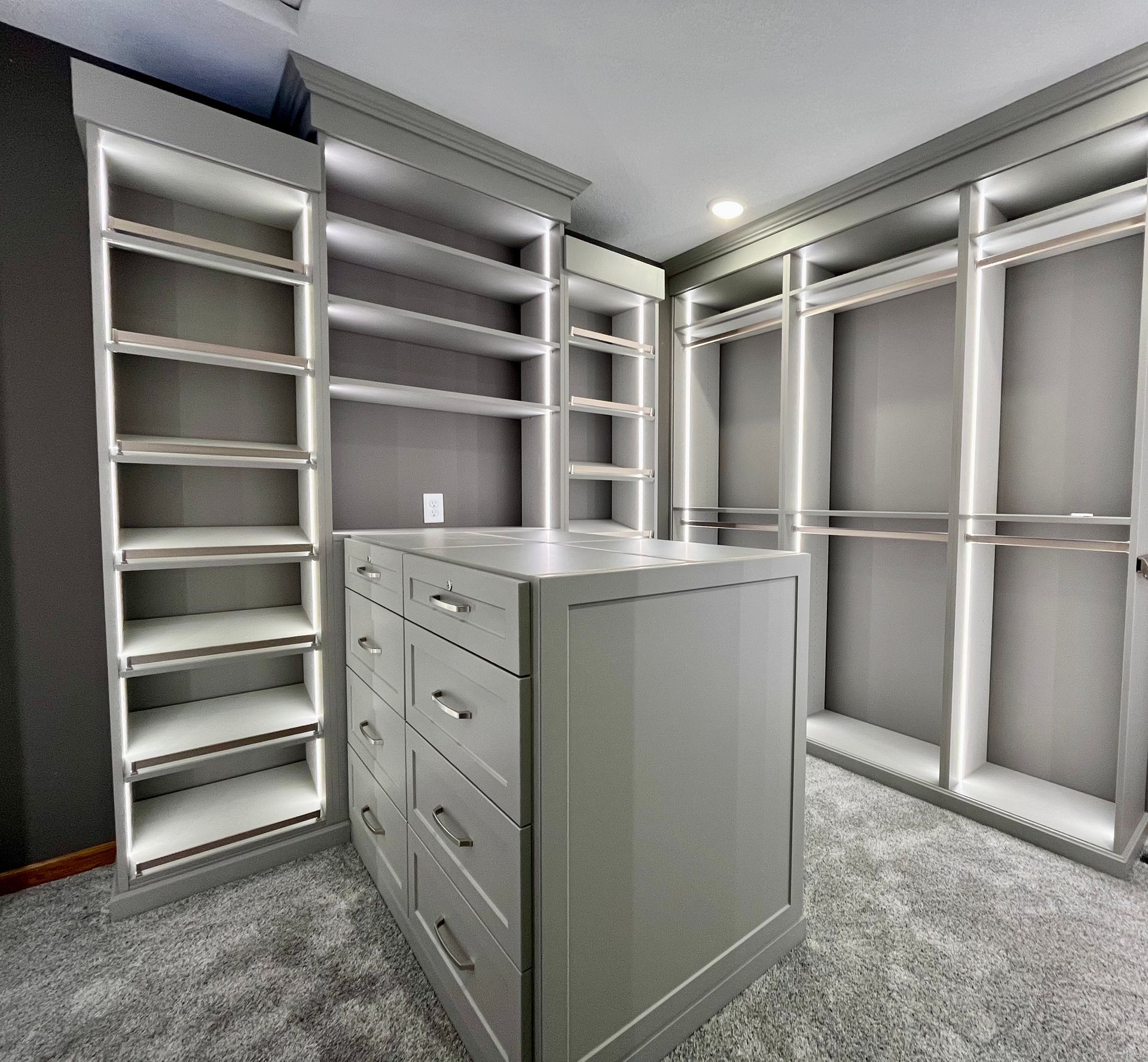 Custom gray walk-in closet with built-in shelves, drawers, and hanging rods on carpeted floor