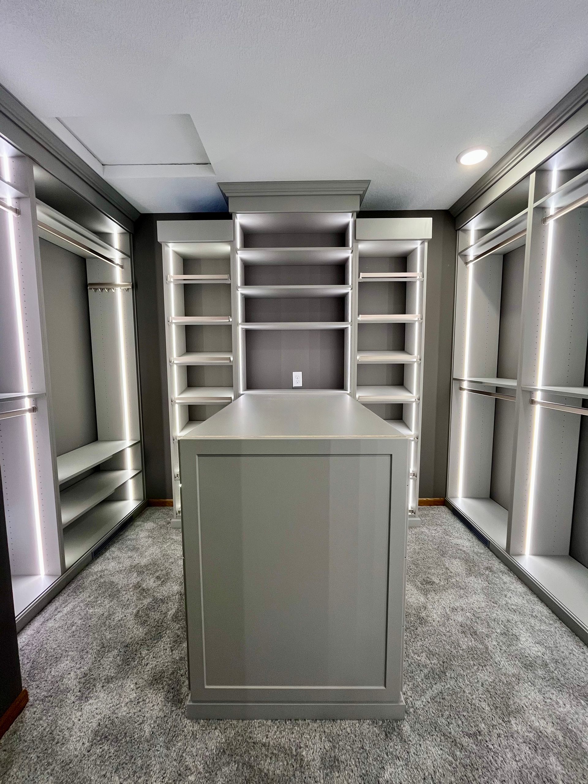 Built-in white shelving and a central cabinet in a carpeted walk-in closet