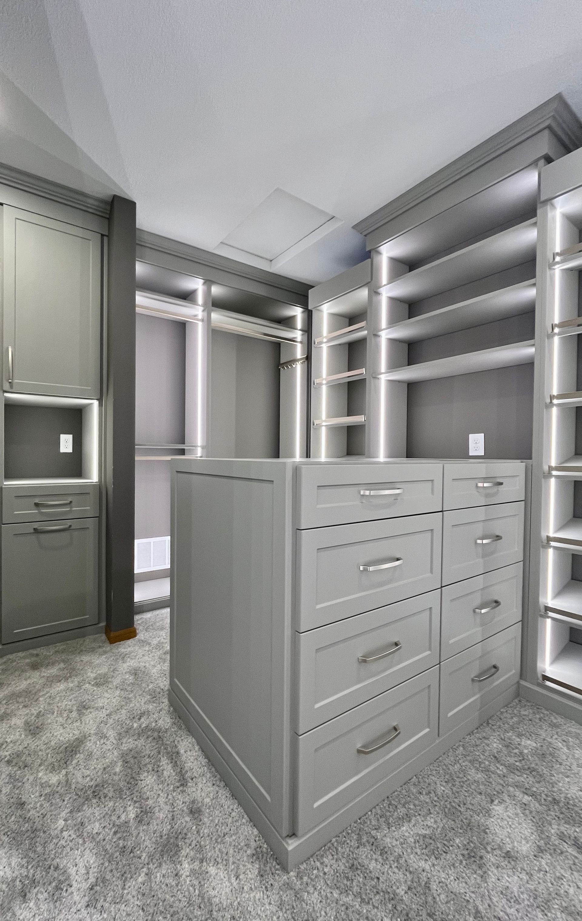 Walk-in closet with white built-in shelves, drawers, and hanging rods on carpeted floor