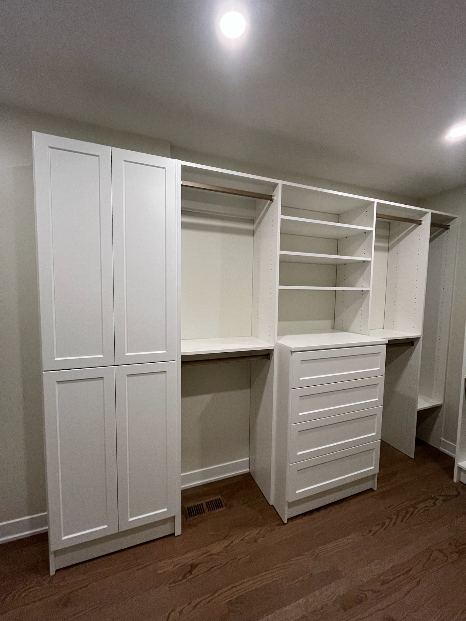 White built-in closet organizers with shelves, drawers, and hanging space in a beige-walled bedroom.