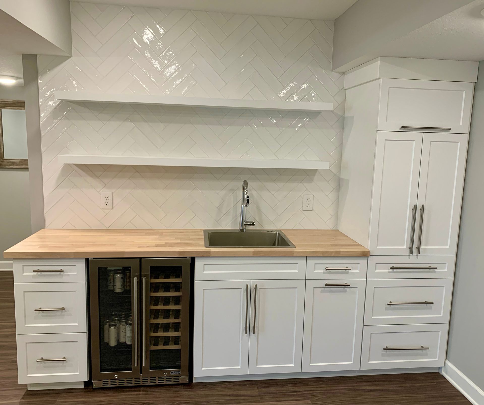 White kitchen with wooden countertop, sink, built-in wine fridge, cabinets, and open shelves against a chevron backsplash