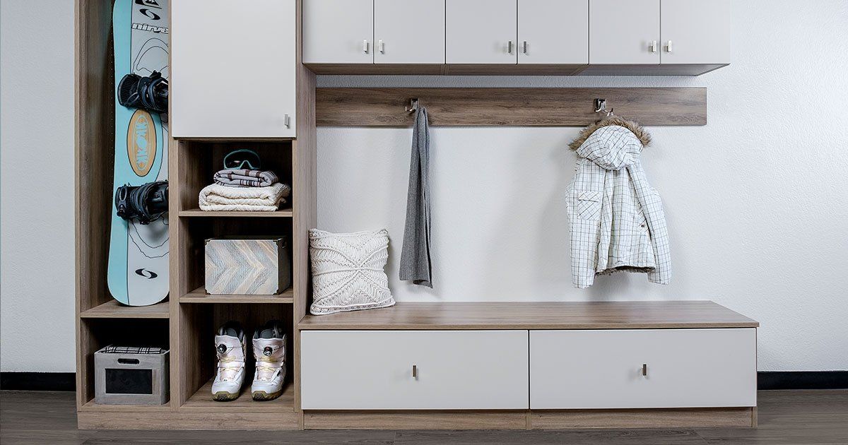 A room with a bench , cabinets , shelves and a snowboard hanging on the wall.