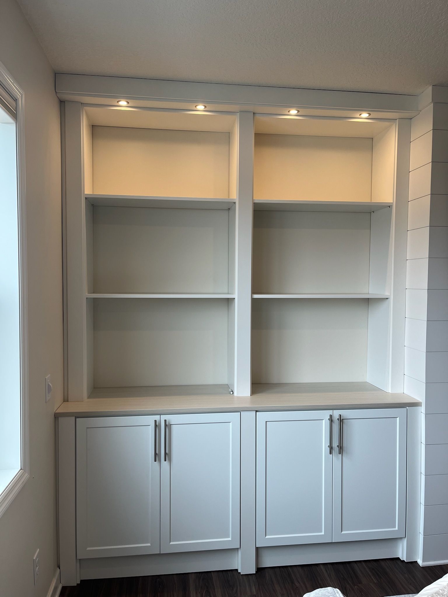 White built-in shelving unit with two cabinets and open shelves in a bright room.