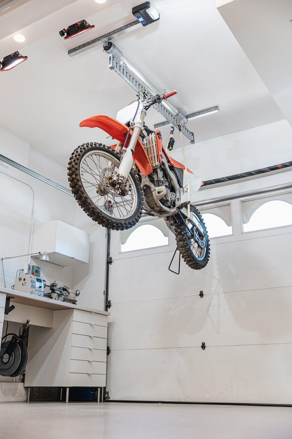A dirt bike is hanging from the ceiling of a garage.