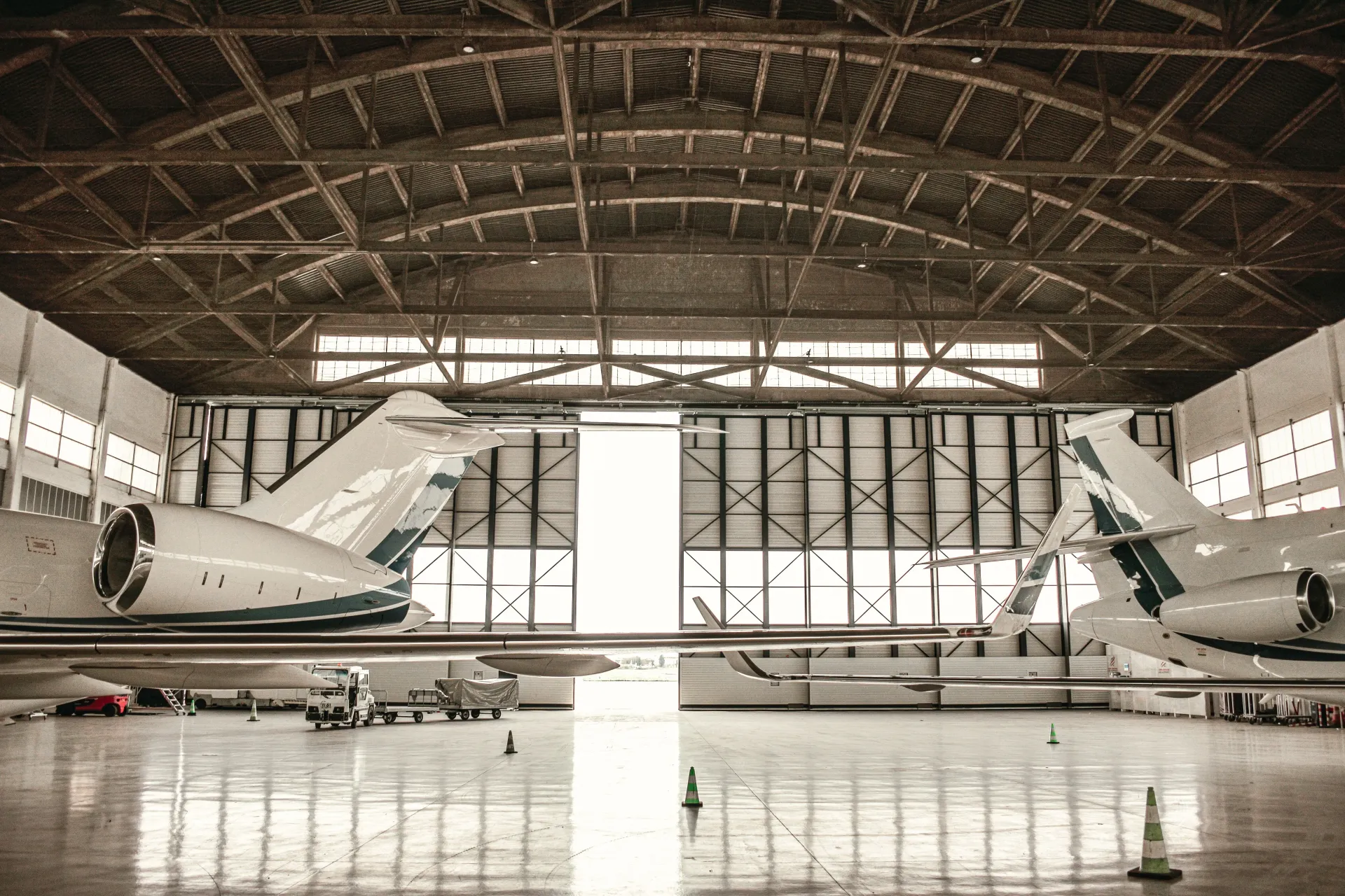 Two private jets parked in a large hangar with a reflective floor and open rear doors