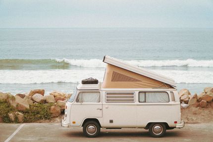 White camper van parked by the ocean with waves and rocks in the background