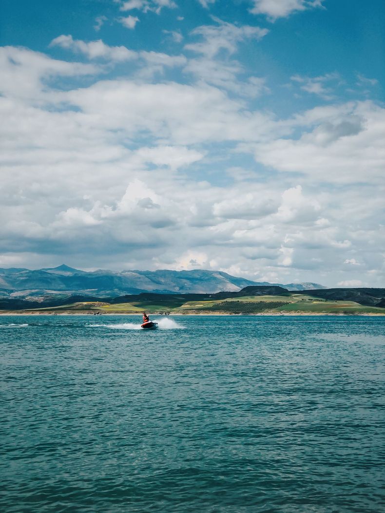 Small boat on blue water with distant mountains under a cloudy sky