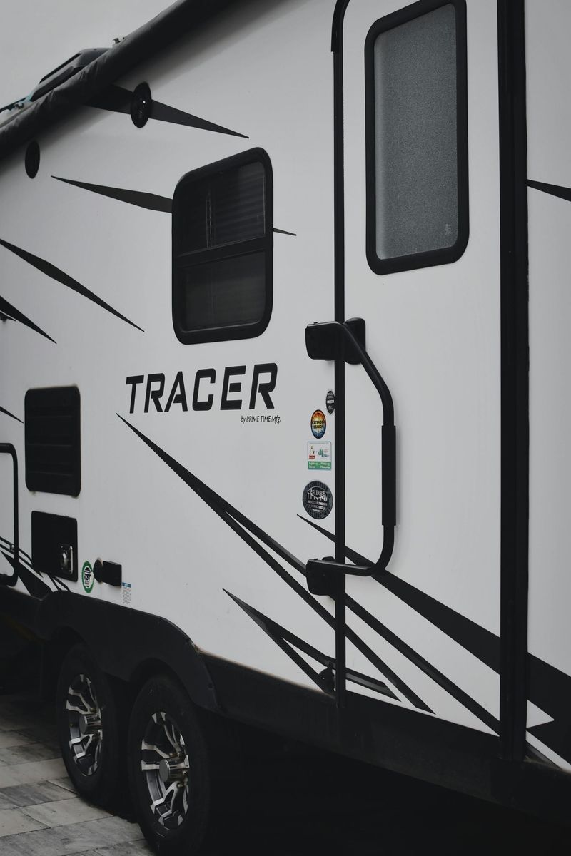 Side view of a white Tracer RV with black accents and windows, parked outdoors.