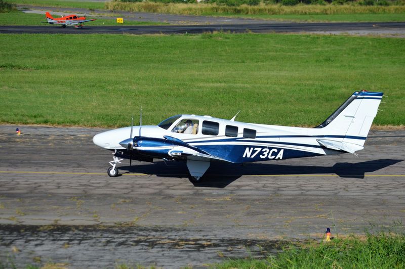 Small white-and-blue single-engine airplane parked on a runway in a grassy airfield