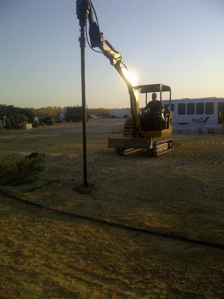 A man is driving a yellow excavator on a dirt road
