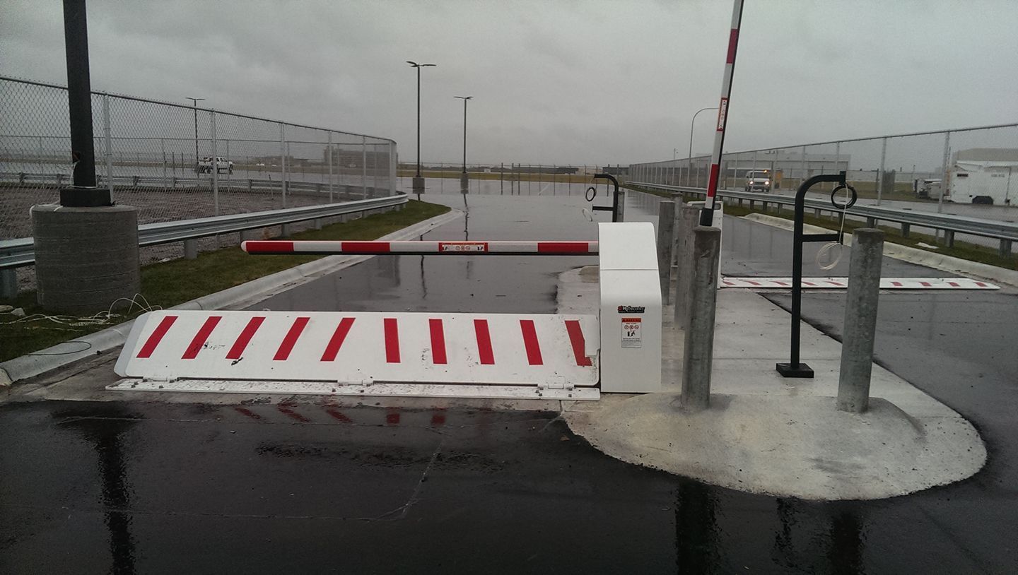 Rainy road barrier with red-and-white stripes, gate arm, and control post on a wet overpass.