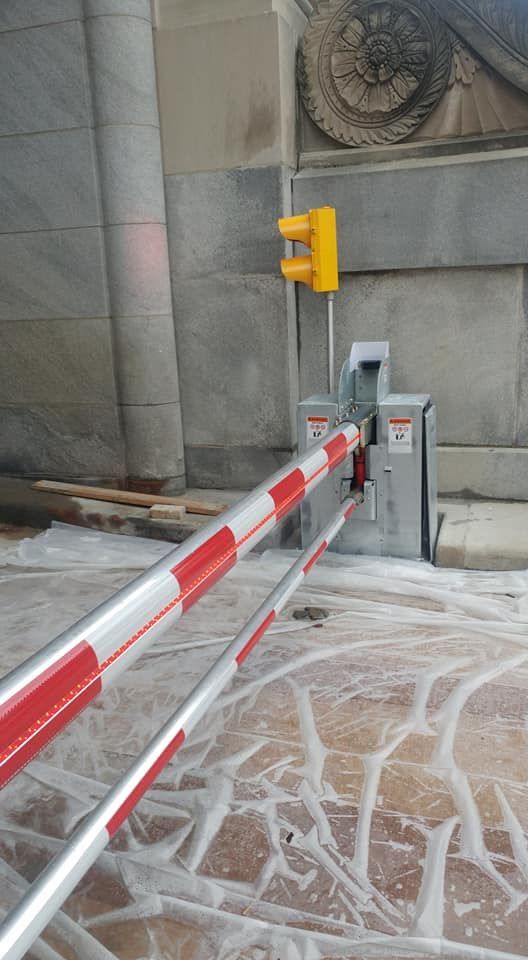 Red-and-white barrier gate blocking a paved entrance beside a gray wall and yellow bollard.