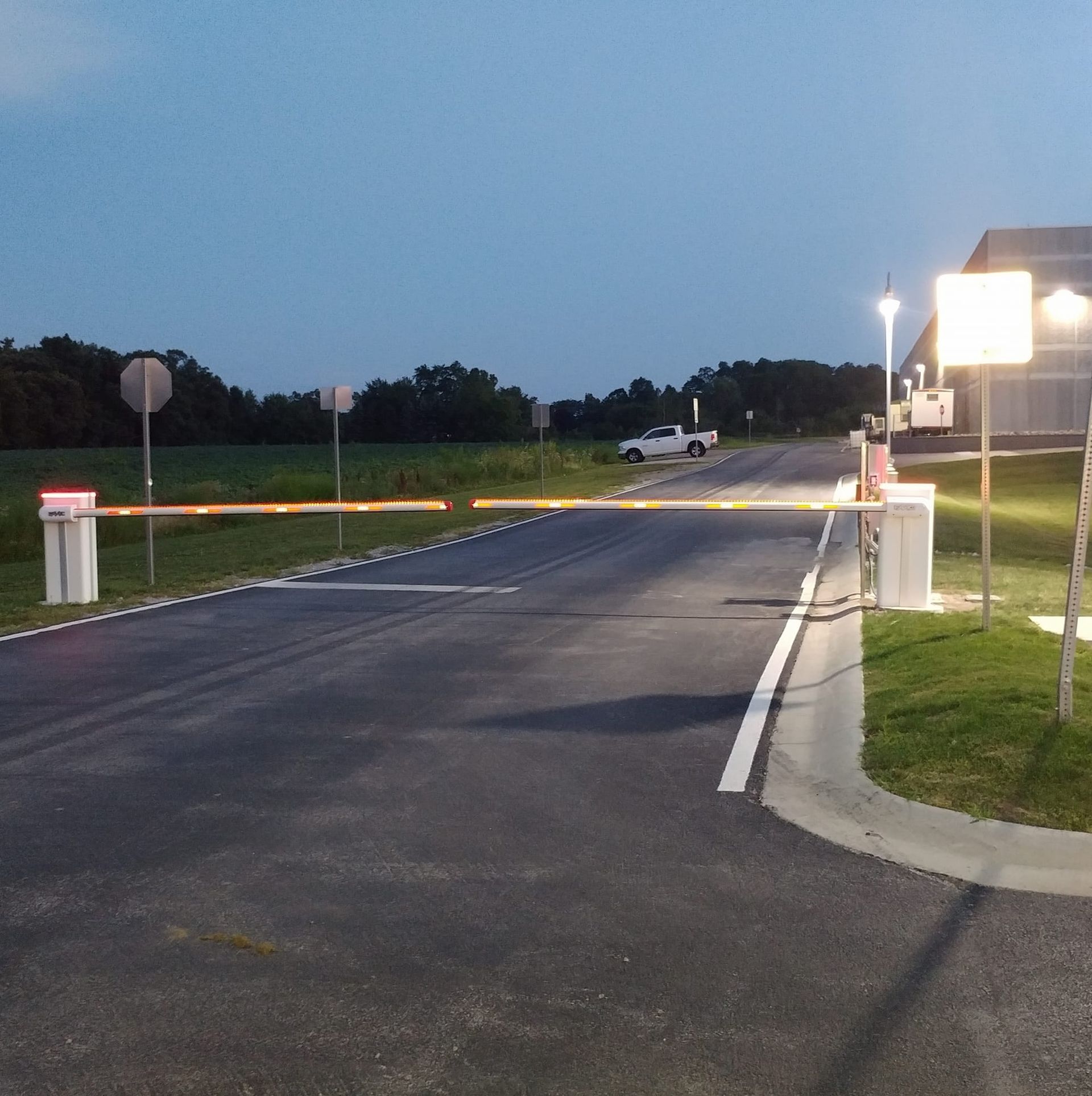 Night view of an empty gated road entrance with white barrier posts and a car in the distance