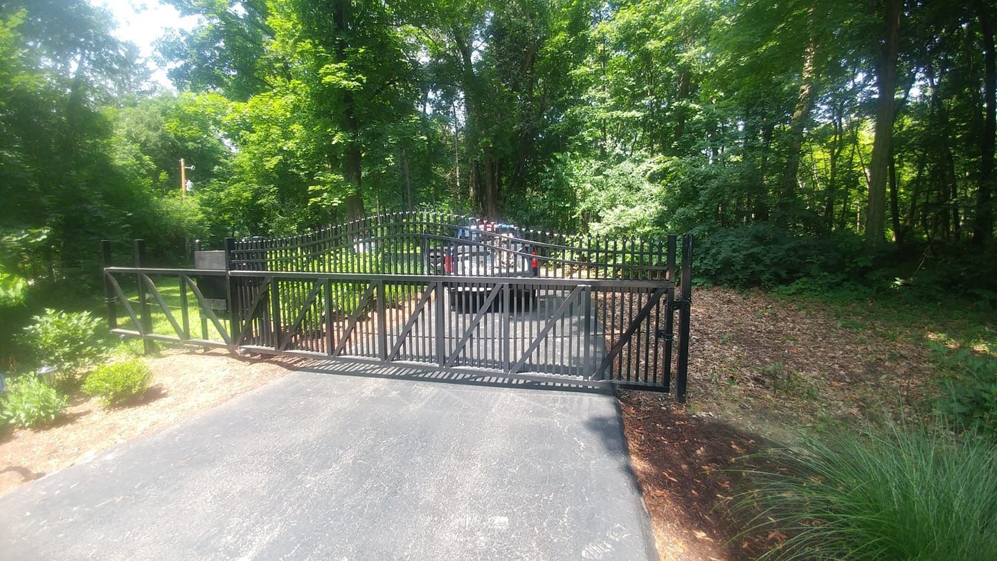 Black metal gate blocks a paved driveway in a wooded park area