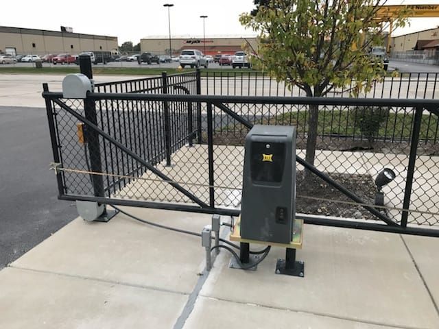 Chain-link gate beside gray utility box on a concrete sidewalk in a parking lot.