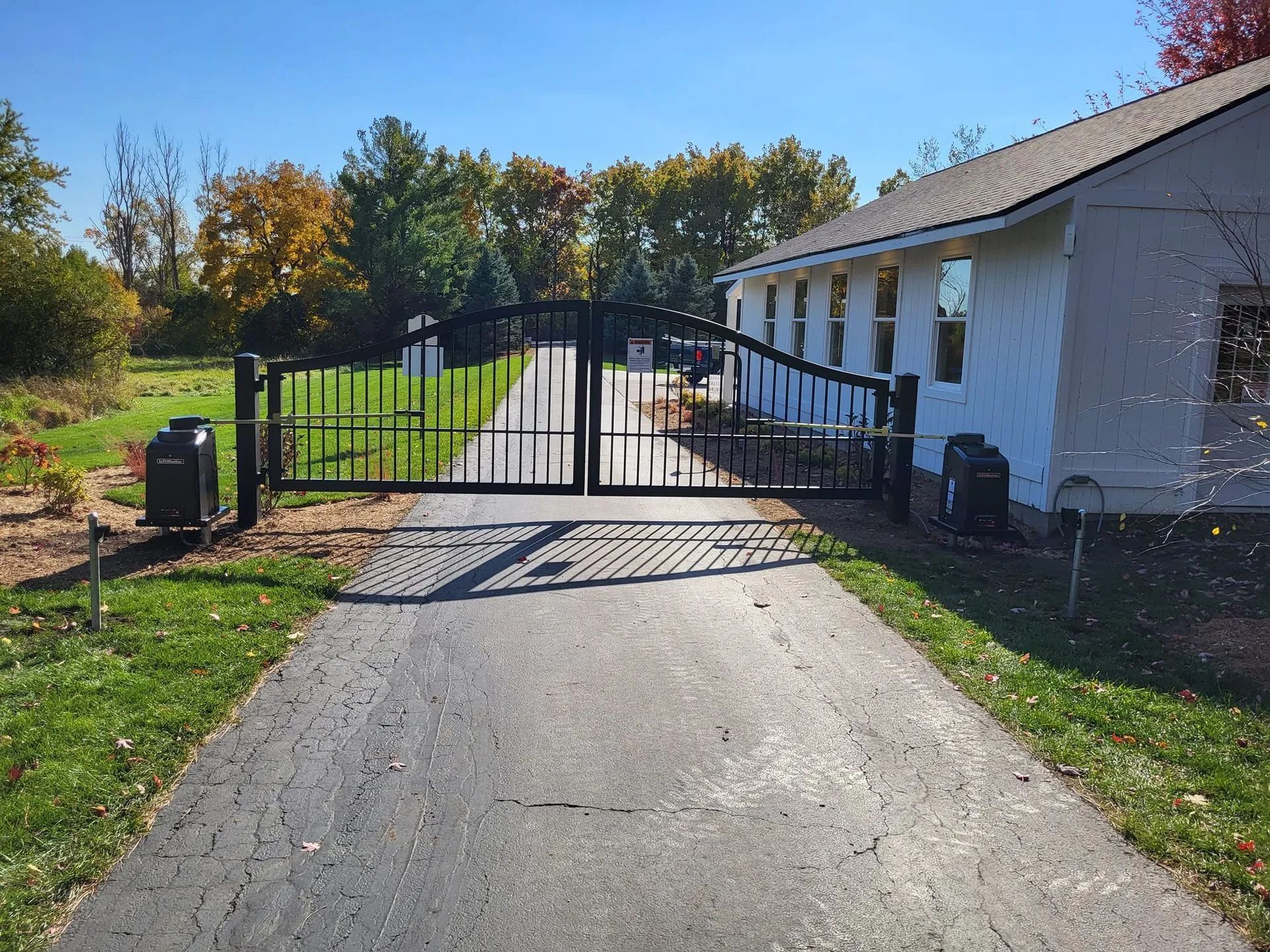 Driveway leading to a black metal gate beside a white house in a sunny rural setting