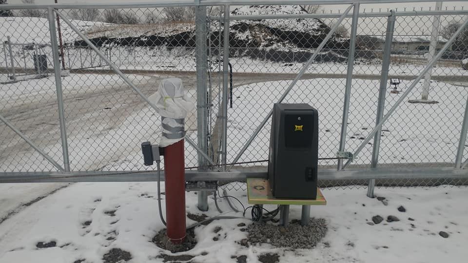 Snowy industrial fenced area with a red post and black utility box near a gate