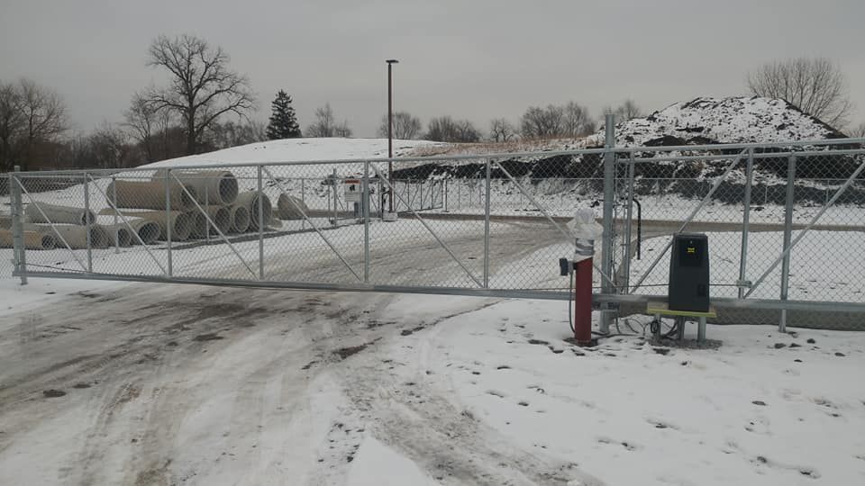 Snow-covered gated entrance with a red fire hydrant and gray utility box under an overcast sky