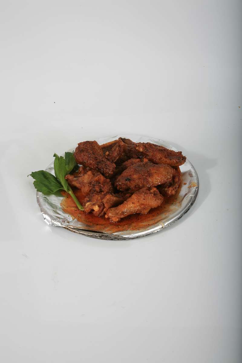 A plate of chicken wings with sauce and parsley on a white surface.