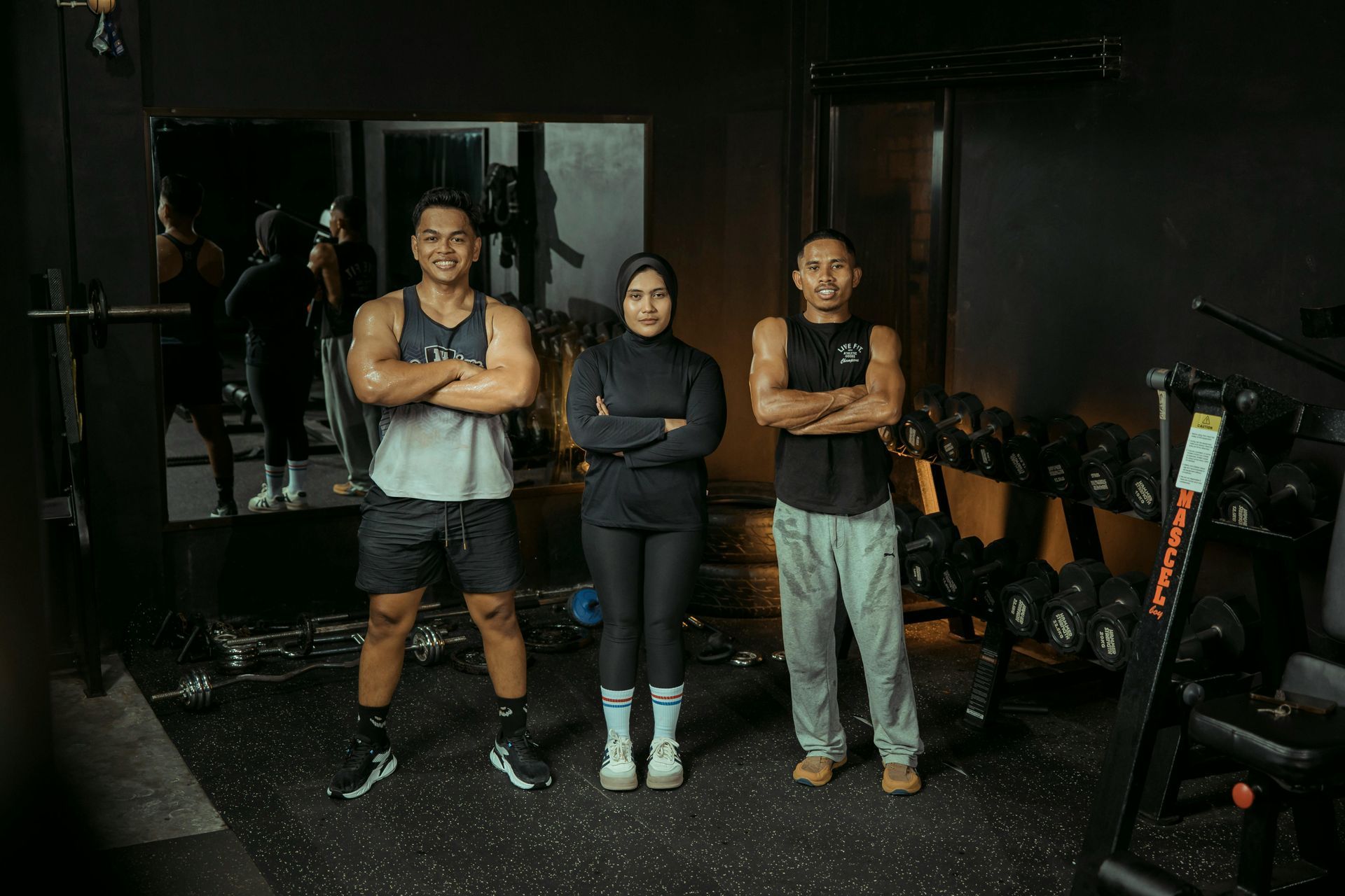 Two men and one woman standing inside a gym with their arms crossed