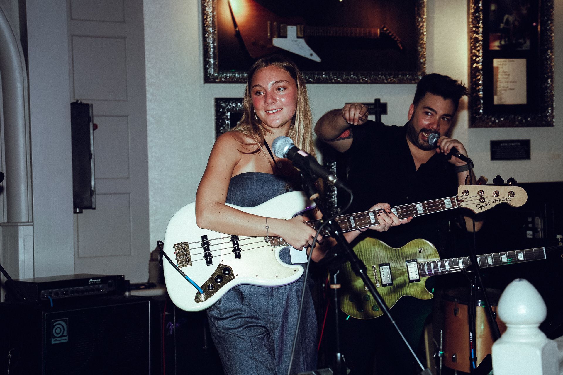 A female bassist and male vocalist perform onstage.