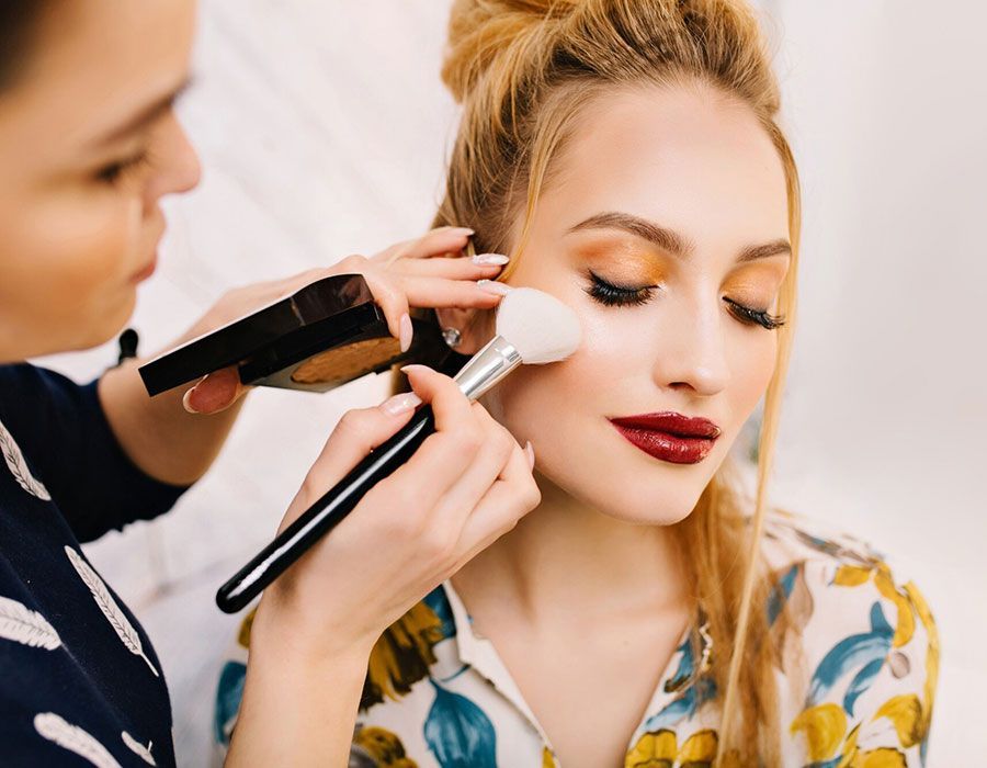 Makeup artist applying powder to a blonde woman with red lipstick