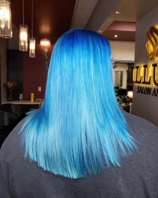 Bright blue shoulder-length hair from behind in a salon setting with hanging lights and wall signage.