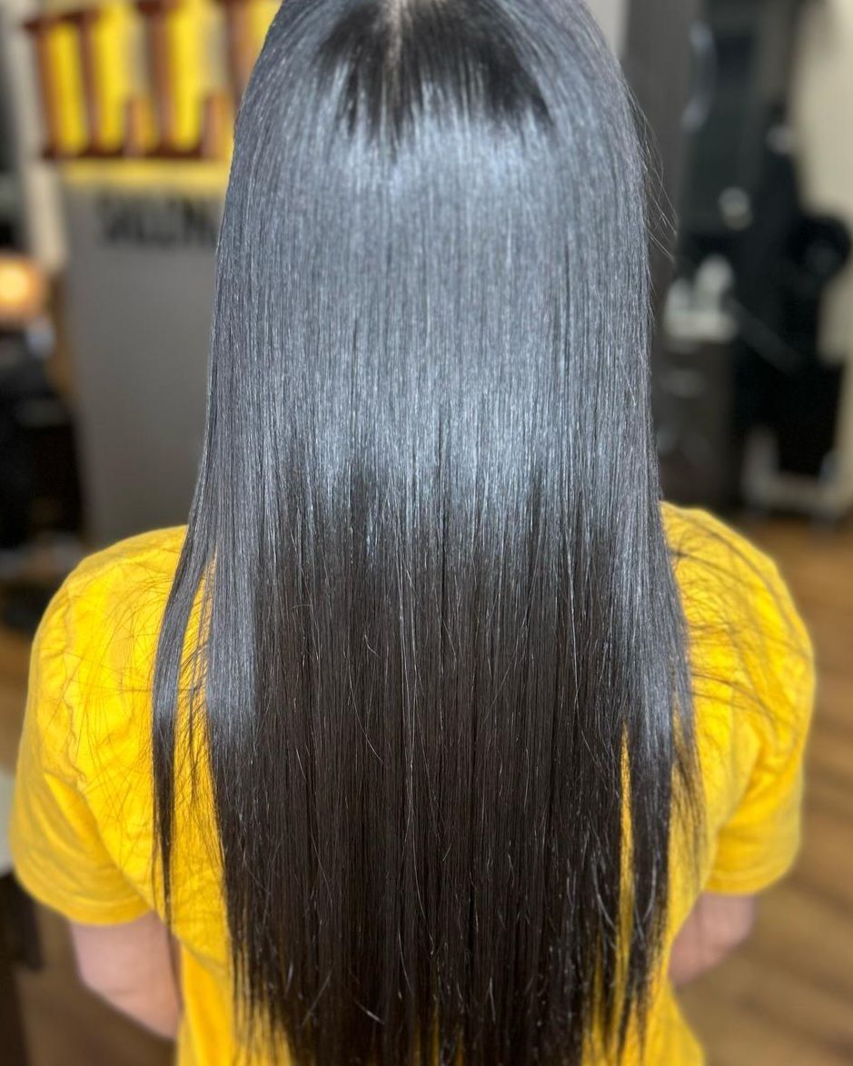 Long straight dark hair from the back, with a yellow shirt in a salon setting.