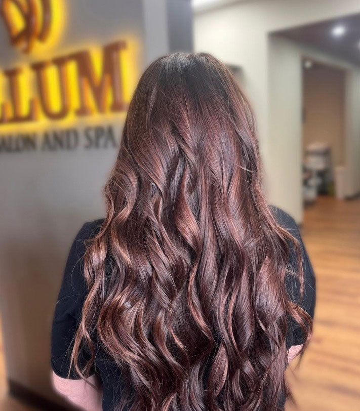 Long wavy brown hair with rose-gold highlights, viewed from behind in a salon.