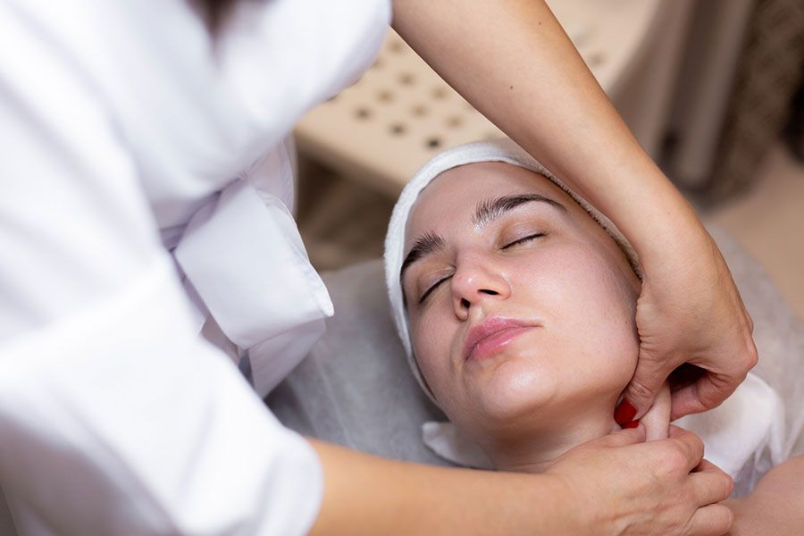 Spa therapist massaging a woman's face with a head wrap while she lies relaxed on a treatment bed