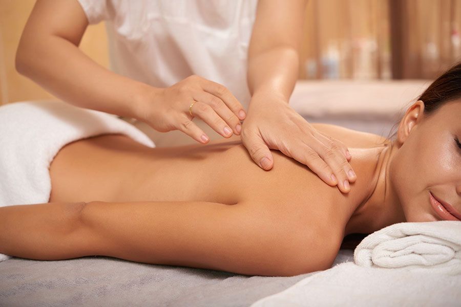 Person receiving a back massage in a spa, lying on a table with a folded towel nearby.