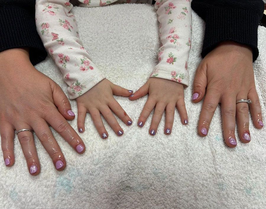 Two adult hands and a child’s hands lined up on a white fuzzy surface, all with pink nail polish