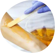 Gloved hand applying wax to a wooden surface with a spatula